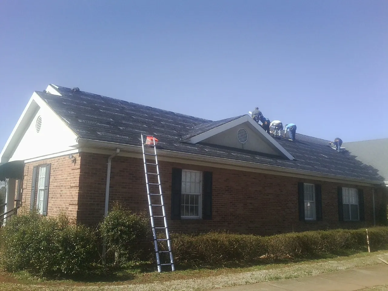 Crew tearing shingles off a brick ranch roof with a ladder set — Emergency Roof Repair work by our crew in Tillson