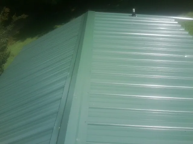 New green metal panels meeting at the ridge of a roof in Tillson