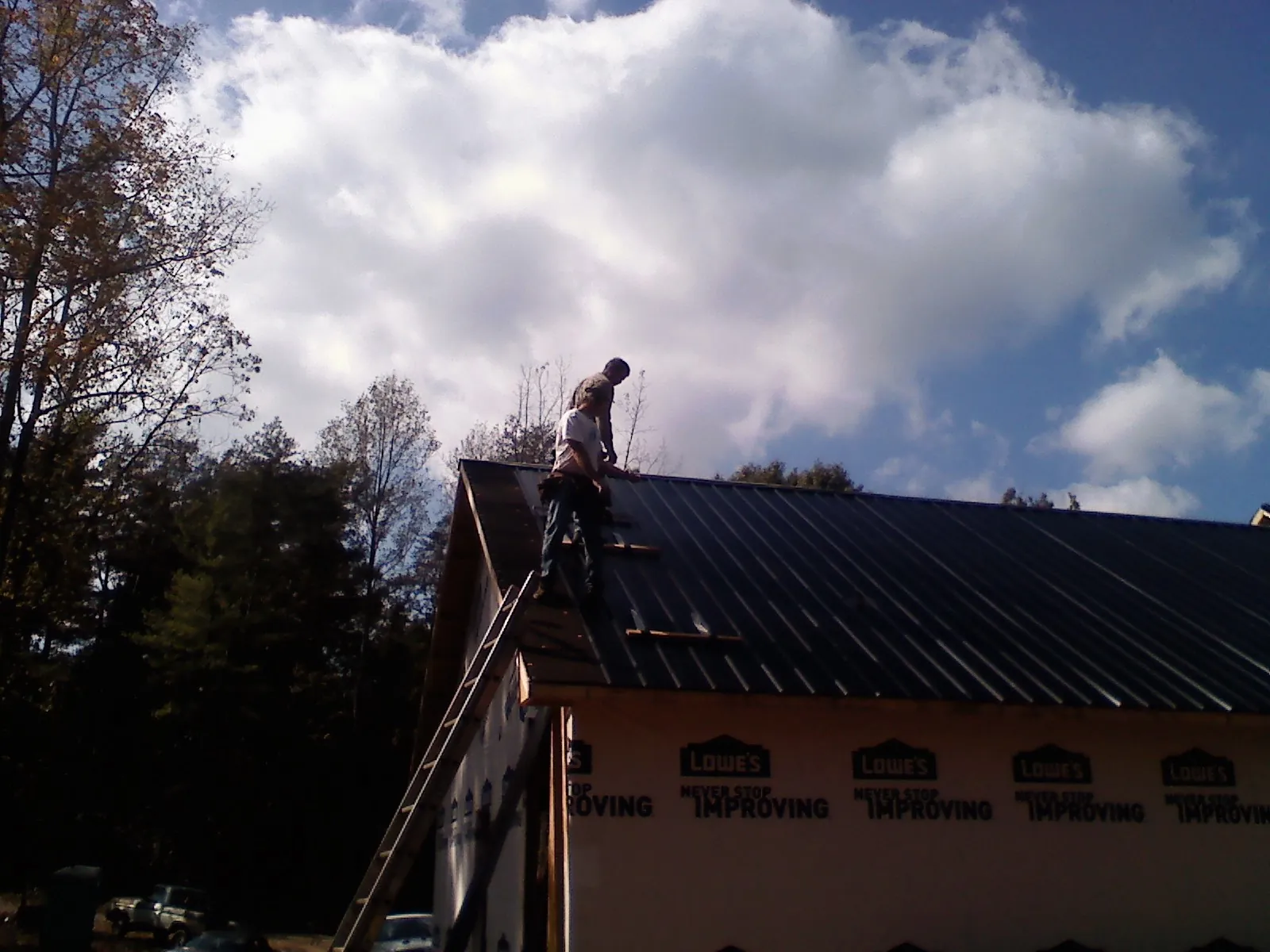 Roofer fastening dark metal panels high against a cloudy sky, from a Roof Inspection job in Tillson
