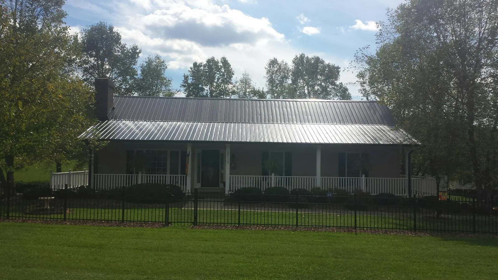 Gray metal roof on a brick ranch with a full width front porch — Gutter Guard Installation work by our crew in Tillson