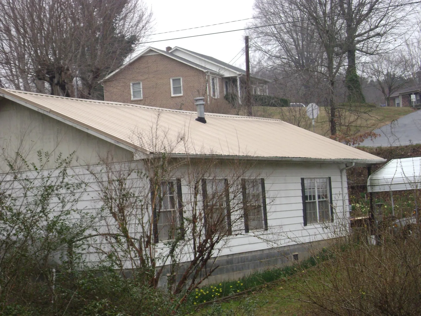 Tan metal roof on a white sided house set into a hillside — Commercial Roofing by Roofing Brothers in Tillson