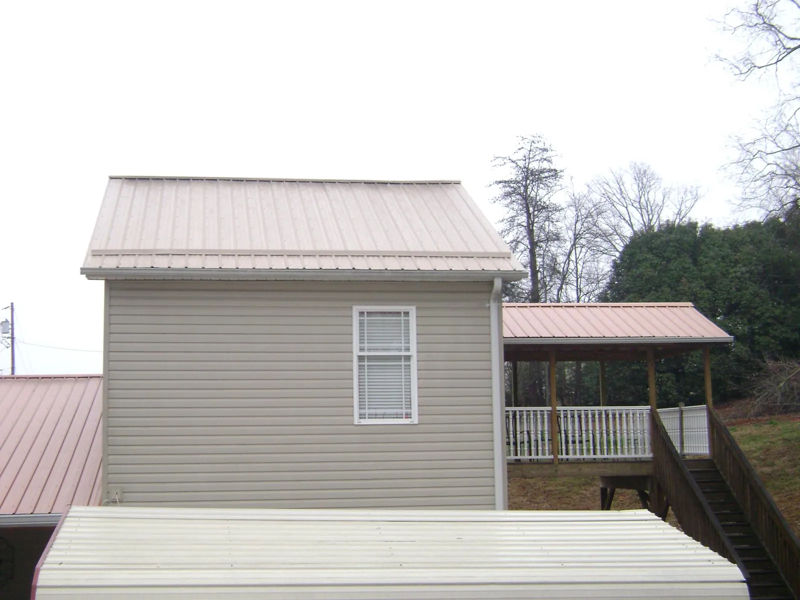 Tan metal roofs on a two story addition and attached porch, from a Roof Replacement job in Tillson